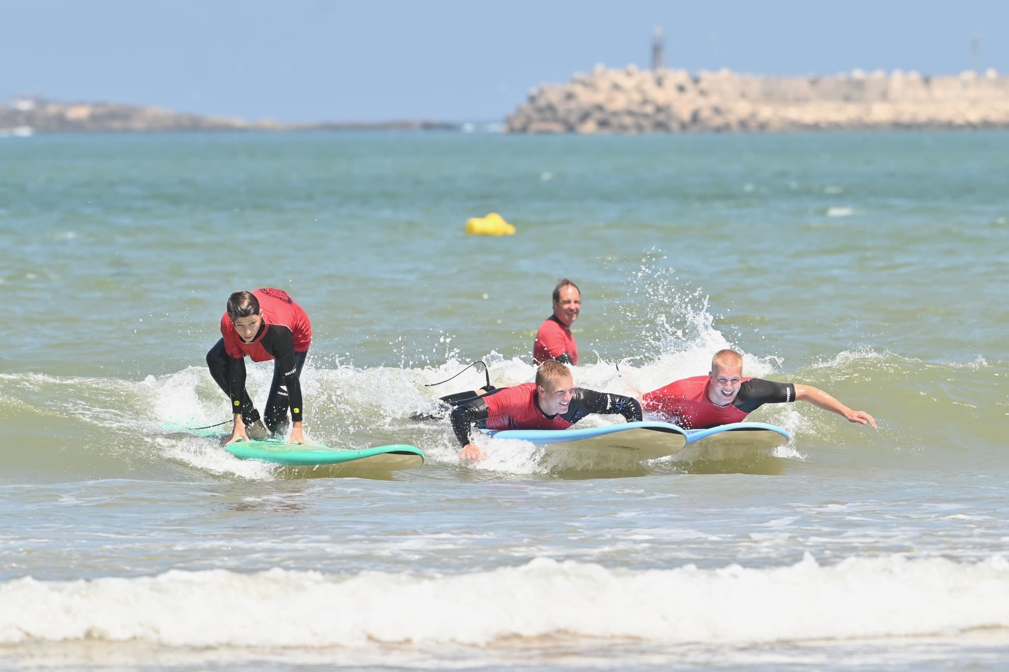 A surfer riding a long, peeling wave at Sidi Kaouki beach near Essaouira. The water is a clear emerald green. The surfer is in a graceful posture. The background features the characteristic Moroccan coastal hills. Soft, warm morning light creates a serene yet energetic atmosphere.
